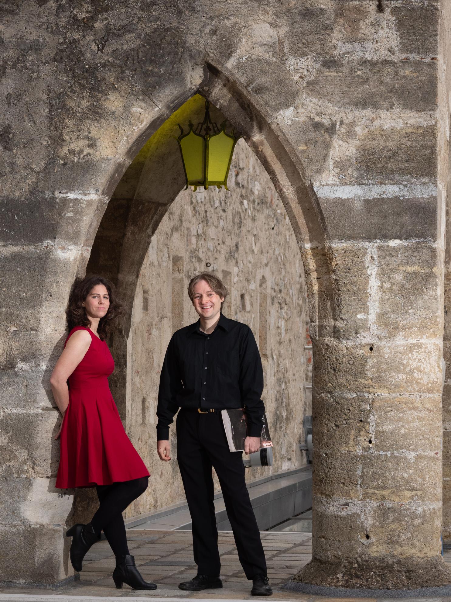 Klavierduo Renate Hudler in einem Torbogen links lehnend und Karl Heinz Grube im Torbogen rechts stehend. Sie hat ein rotes knielanges Kleid an; er trägt schwarzes Hemd und Hose und Noten lässig mit der hängenden linken Hand. Im spitzzulaufenden Torbogen hängt oben eine gelbglasige viereckige Laterne.